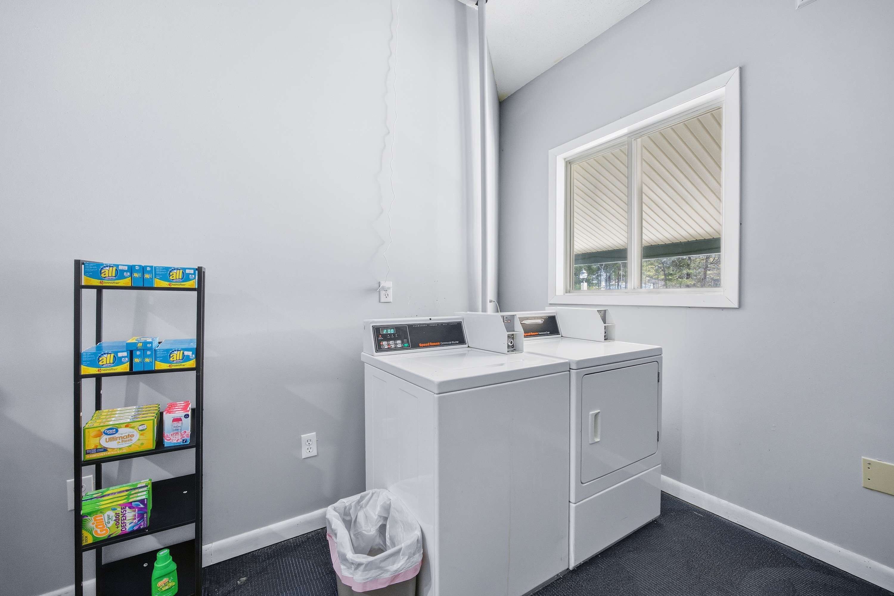 A laundry area with a washing machine, a shelf with detergent, and a window.