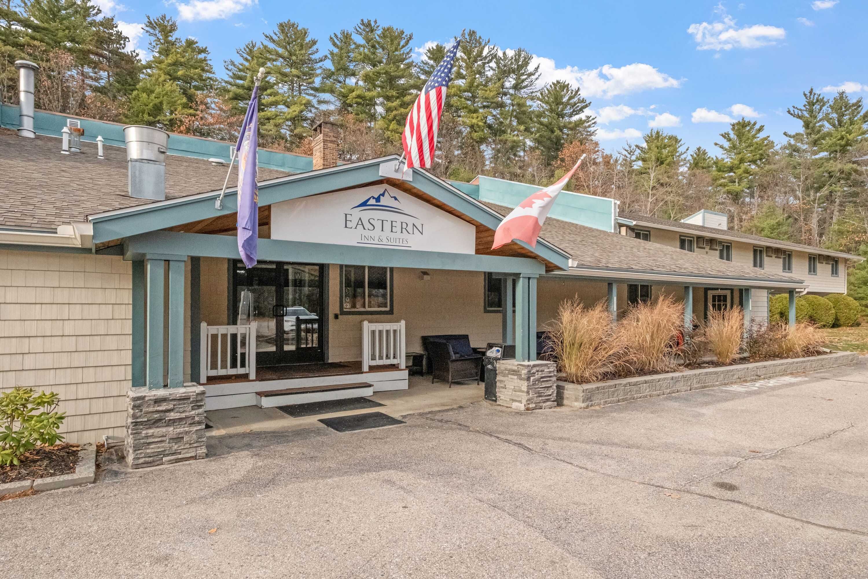 A building with a sign reading 'Eastern Inn & Suites,' a flagpole with an American flag, and a flag with a mountain design.
