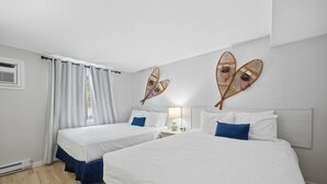 A hotel room with two beds, a window with curtains, a wall-mounted fan, and a nightstand with a lamp. - Eastern Inn Peaked Mountain Escape (North Conway)
