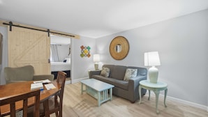 A living room with a wooden dining table, a sofa, a coffee table, and a lamp. - Eastern Inn Peaked Mountain Escape (North Conway)