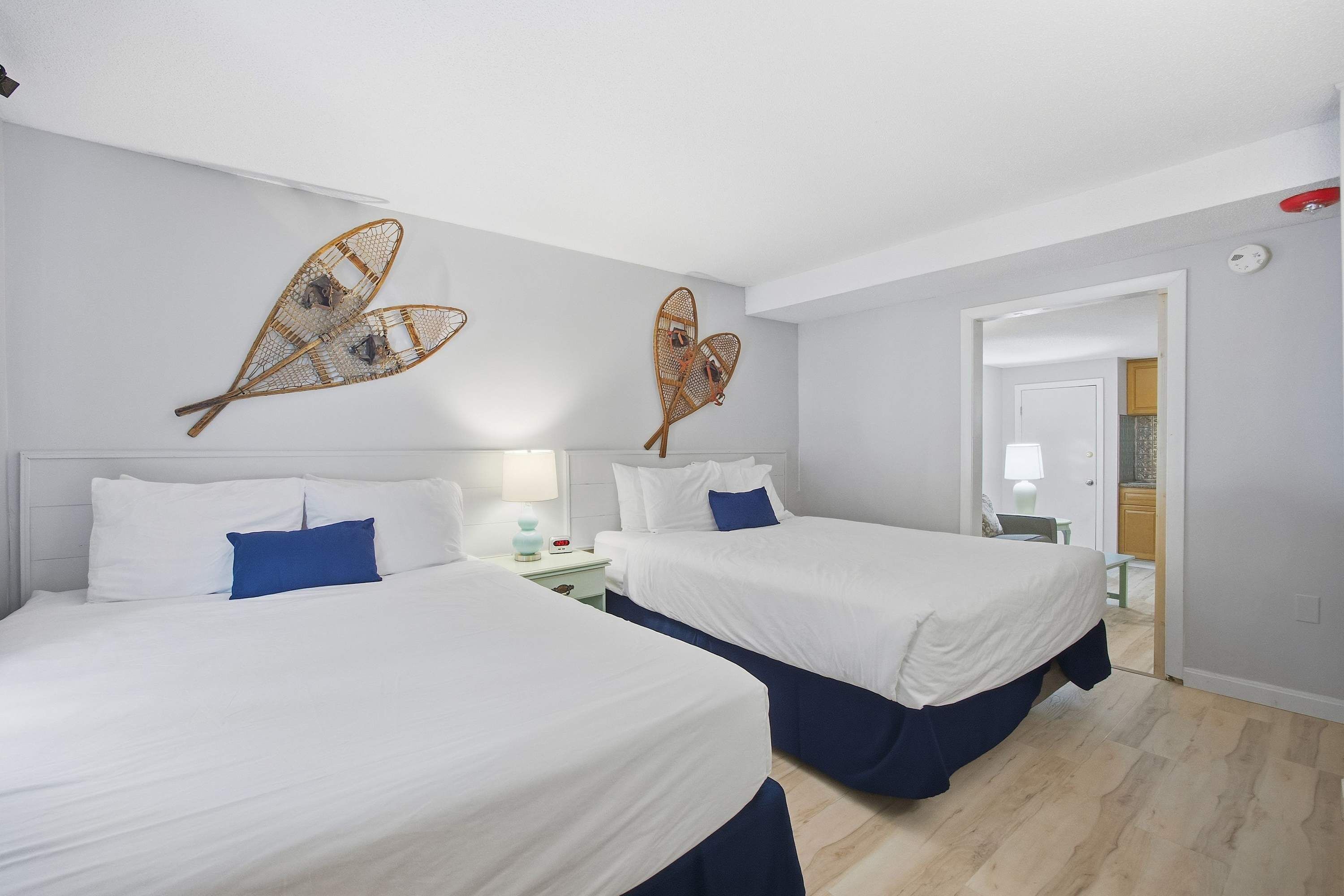 A hotel room with two beds, a nightstand, a lamp, and decorative wall art.