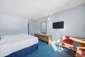 Ein Hotelzimmer mit Bett, einem Holzkoffer, einem Fernseher, einem Schreibtisch mit Stuhl und einem blauen Teppich.