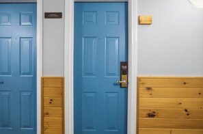 Eine blaue Tür mit einem Schild ‚Nichtraucher‘, eine Holztür mit einer Nummertafel und eine Holzwand.