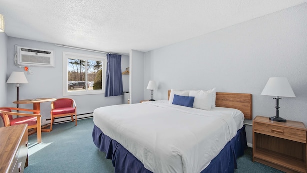 A hotel room with a bed, two bedside tables with lamps, a desk with a chair, and a window with curtains. - Eastern Inn Scenic Railway Suite (North Conway)