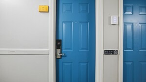 Une porte bleue avec une pancarte indiquant « Merci de ne pas fumer », un interphone et un interrupteur sur le mur.