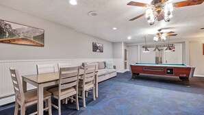 A room with a pool table, dining table, and chairs, a ceiling fan, and artwork on the walls. - Eastern Inn Ridge Retreat Suite (North Conway)