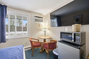 A compact room with a bed, a small table with two chairs, a microwave, a TV, and a window with curtains. - Eastern Inn Ridge Retreat Suite (North Conway)