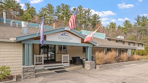 A building with a sign reading 'Eastern Inn & Suites,' a flagpole with an American flag, and a flag with a mountain design. - Eastern Inn Ridge Retreat Suite (North Conway)