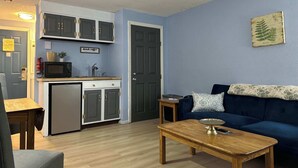 A compact living space with a kitchenette, a blue sofa, a wooden coffee table, and a small side table. - Eastern Inn Hemlock Hideout (North Conway)