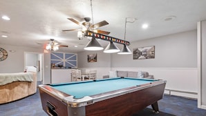 A pool table in a room with a ceiling fan, pendant lights, a clock, and a framed picture on the wall. - Eastern Inn Hemlock Hideout (North Conway)