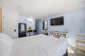 Ein Schlafzimmer mit Bett, Schreibtisch, Kühlschrank, Fernseher und einer Tür.