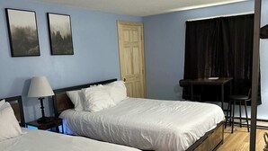 Una habitación de hotel con dos camas, un escritorio, una silla, una lámpara y una puerta.