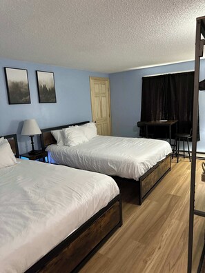 A hotel room with two beds, a desk, a chair, a lamp, and a door. - Eastern Inn Scenic Retreat NH (North Conway)