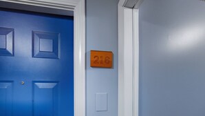 Una puerta azul con una placa que indica la habitación 216, un interruptor de luz y una pared blanca.