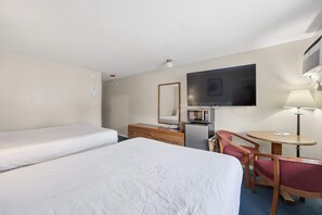 Una habitación de hotel con dos camas, un escritorio con computadora, un televisor y una lámpara.