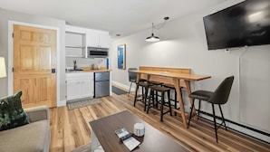 Un espacio habitable compacto con kitchenette, zona de comedor, televisor montado en la pared y sofá.