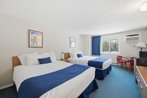 Ein Hotelzimmer mit zwei Betten, einem Schreibtisch, einem Stuhl, einem Vorhangfenster und einer Wand-Klimaanlage.