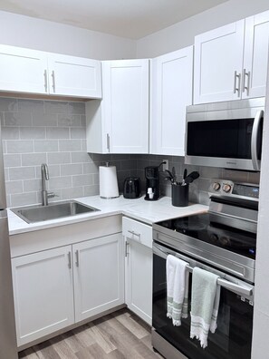 A modern kitchen with white cabinets, a stainless steel sink, a microwave, a coffee maker, and an oven. - World Cup Stay | Near Beach. Apt # 7 (Fort Lauderdale)