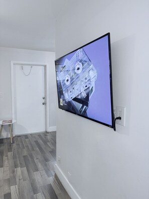 Ein Zimmer mit einem an der Wand befestigten Flachbildfernseher, einer weißen Tür und einem kleinen Tisch mit einem Buch.