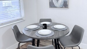 Un comedor con una mesa redonda, cuatro sillas grises y un cuadro en la pared.