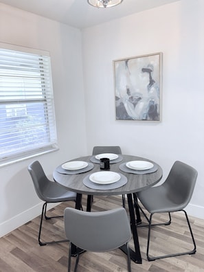 Ein Essbereich mit einem runden Tisch, vier grauen Stühlen und einem Bild an der Wand.