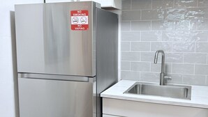 Una cocina con refrigerador de acero inoxidable, armarios blancos, salpicadero de azulejos y un lavamanos.