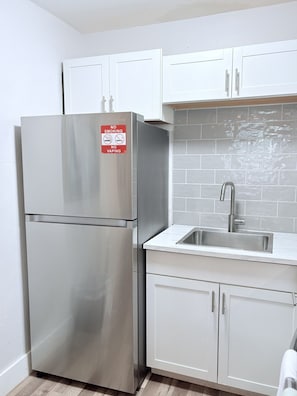 Eine Küche mit einem Edelstahlkühlschrank, weißen Schränken, einer gefliesten Spritzschutzwand und einem Spülbecken.
