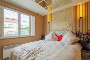 A bedroom with a large window, a bed with white bedding, and a decorative wall panel.