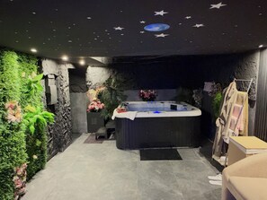 Un'area spa con vasca idromassaggio, vegetazione artificiale e un soffitto a cielo stellato.