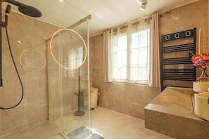A modern bathroom with a glass-enclosed shower, a vanity with a towel rack, and a window with curtains.