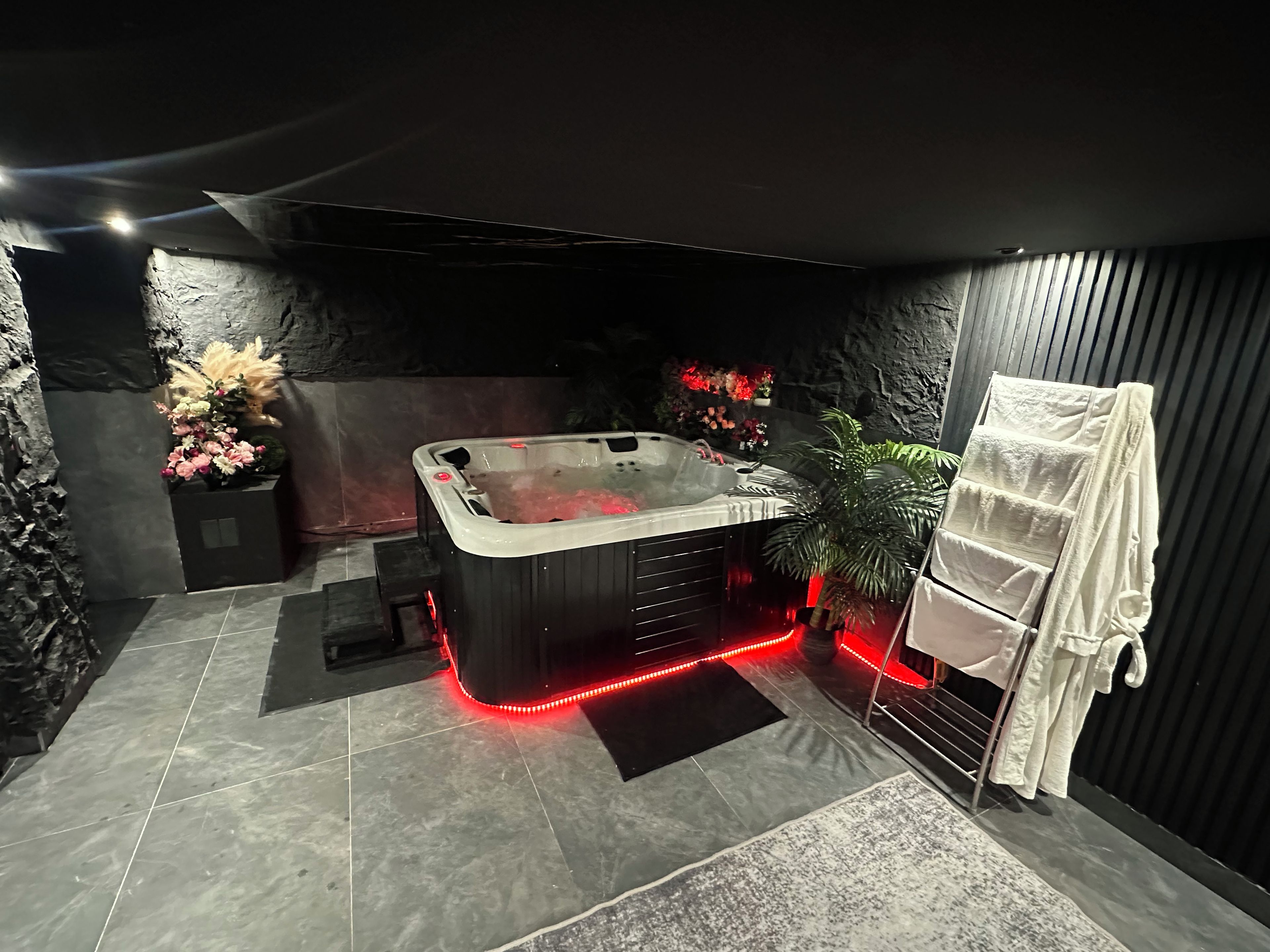 Een moderne badkamer met een whirlpool, rode LED-verlichting, een handdoekhouder en decoratieve bloemen.