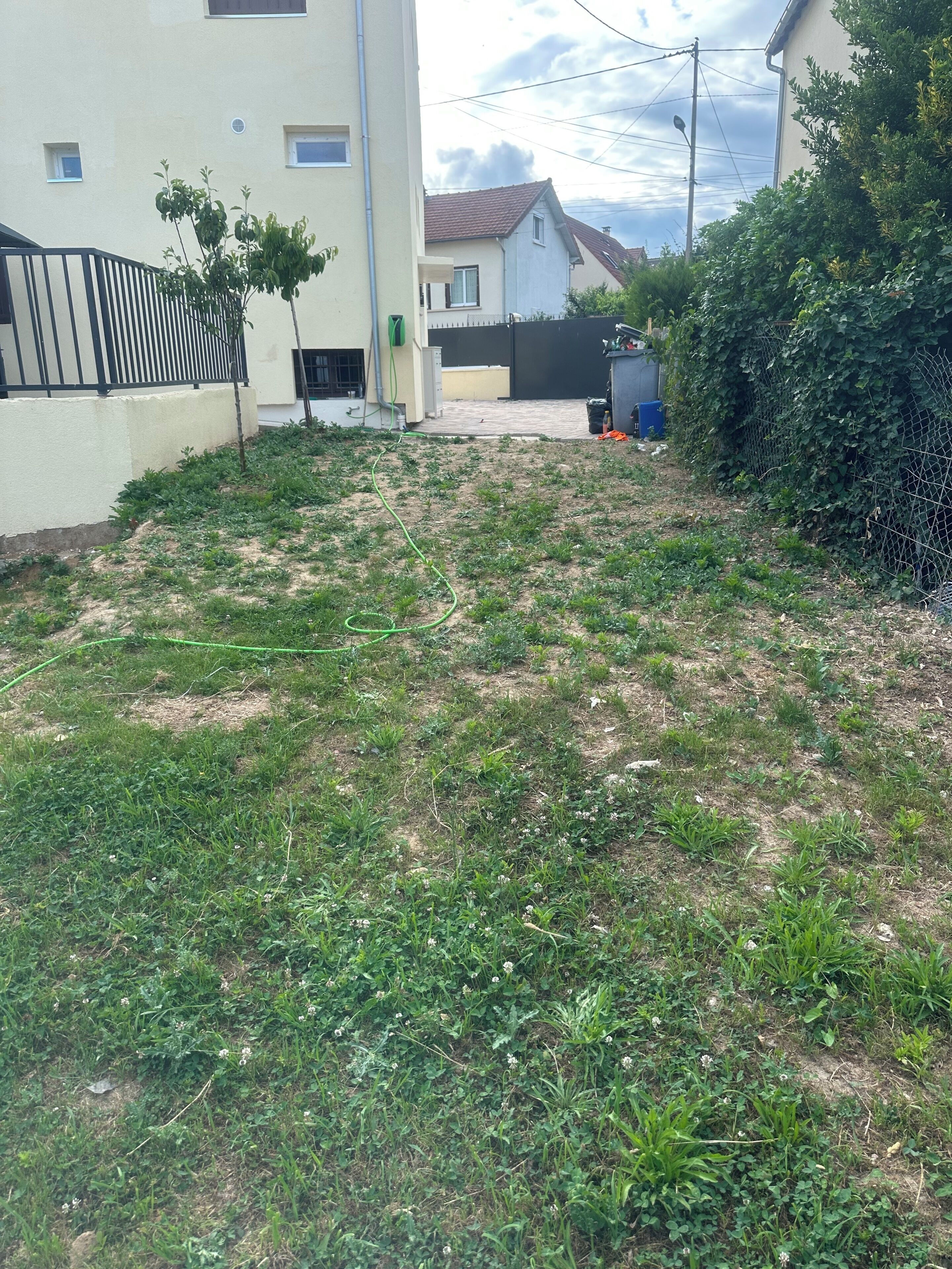 Un quartier résidentiel avec une cour verdoyante, une clôture en métal noir et un bâtiment à la façade blanche.