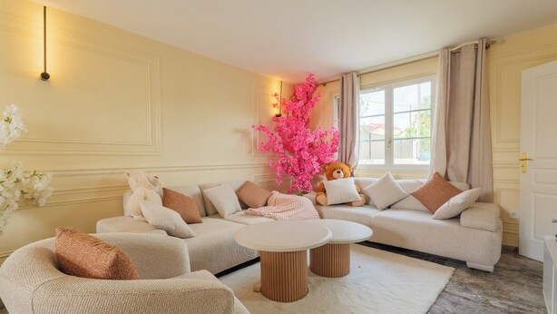 A living room with a sofa, two armchairs, a coffee table, and a decorative pink plant.