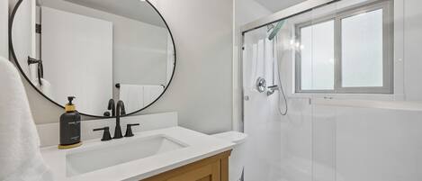 A bathroom with a white sink, a mirror, a toilet, and a shower.