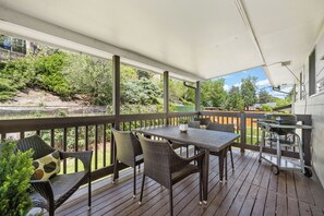 Eine überdachte Terrasse im Freien mit Tisch, Stühlen, einem Grill und Blick auf die umliegende Natur.