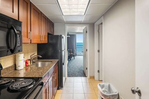 A kitchen with a microwave, stove, sink, and cabinets. A trash can is visible in the foreground. - Oceanfront Unit with Private Balcony and Pool Access (Myrtle Beach)