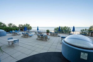 Ein Poolbereich auf dem Dach mit Liegestühlen und Sonnenschirmen mit Blick aufs Meer.
