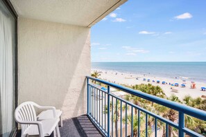 A balcony with a view of a beach, a white chair, and a blue railing. - Oceanfront Unit with Private Balcony and Pool Access (Myrtle Beach)