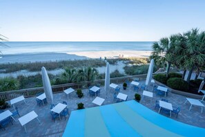 An outdoor seating area with tables and chairs, overlooking a beach and ocean. - Oceanfront Unit with Private Balcony and Pool Access (Myrtle Beach)