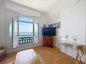 Ein Zimmer mit großem Fenster, Fernseher, Holzschrank und einem dekorativen Tisch.