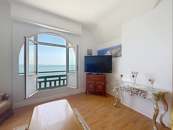 Ein Zimmer mit großem Fenster, Fernseher, Holzschrank und einem dekorativen Tisch.