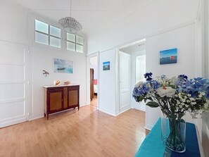 Ein geräumiges Zimmer mit Holzboden, einem Holzschrank, einer Vase mit Blumen und einer Chandelüster.