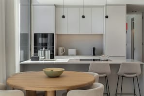 A modern kitchen with white cabinetry, a round wooden table, and bar stools.