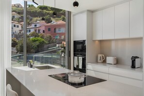 A modern kitchen with a large window, a built-in stove, and a view of a hillside.