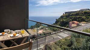 Een balkon met een ontbijttafel, met uitzicht op een kustweg en gebouwen.