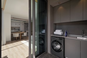 A modern kitchen with a built-in washer, a dining area, and a glass door leading to a balcony.