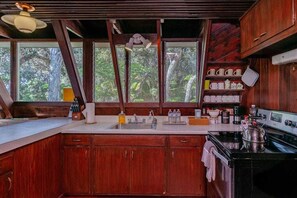 A kitchen with wooden cabinets, a sink, a stove, and a window with a view of trees.