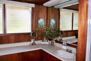 A bathroom with wooden paneling, a white sink, two mirrors, and a vase with flowers.
