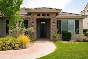 A house with a stone facade, a black door, and a well-maintained lawn. - Stunning 5BR Oasis • Hot Tub • Casita • Hurricane (Hurricane)