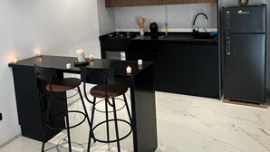 A modern kitchen with a black countertop, two bar stools, a refrigerator, and a wooden cabinet. - Luxurious Apartment in La Soukra Comfort Meets Convenience (Tunis)